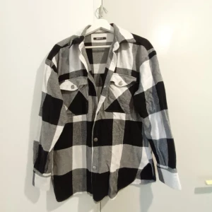 Overshirt i svartvitt rutigt mönster - Stilren overshirt med stora svarta och vita rutor. Klassisk krage, två bröstfickor med lock och knappar framtill. 