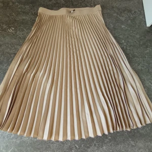 Beige plisserad långkjol -  Beige midikjol med plisserad design och bred midjeresår. 