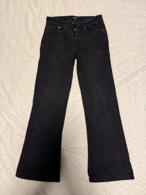 Svarta bootcut jeans med fem fickor - Säljer ett par svarta bootcut jeans med klassisk femficksdesign och hällor för skärp. Jeansen har en något utsvängd passform nertill och stängs med dragkedja och knapp. Perfekta för dig som gillar en tidlös och avslappnad stil.