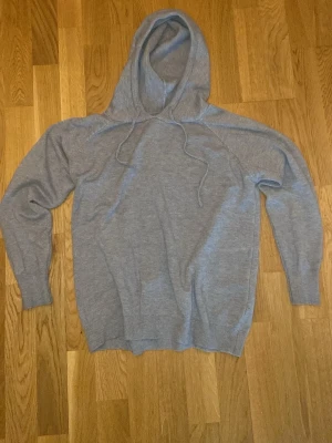 Ljusgrå Marino-ull hoodie med huva - En enkel och stilren ljusgrå hoodie med huva och dragsnören. Tillverkad i marinoull  material och har ribbade muddar vid ärmslut och nederkant. Perfekt för en avslappnad look och passar till det mesta i garderoben.
