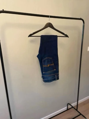Nudie jeans med stretch - Säljer ett par mörkblå nudie jeansmed klassiska fem fickor och kontrastsömmar. Jeansen har bra  passform och är tillverkade i ett stretchigt denimtyg som sitter snyggt och bekvämt. Perfekta till en avslappnad eller trendig look. L 32