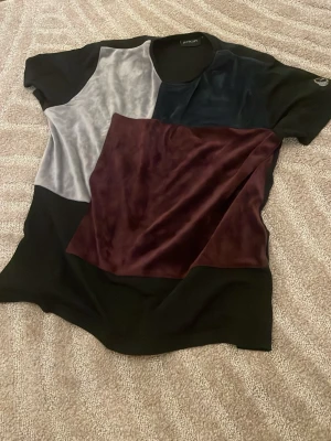 Lavichy T- shirt - Unik t-shirt från Lavichy med patchwork-design i svart, vinrött och grått. T-shirten har korta ärmar och är tillverkad i en mix av bomull och sammet för en lyxig känsla. Perfekt för dig som vill sticka ut med en cool och modern look.