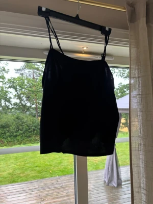 Svart linnetopp med tunna axelband - Säljer en enkel och stilren svart linnetopp med tunna axelband. Toppen har en rak passform och ärmlös design, perfekt för varma dagar eller som layering-plagg. Passar dig som gillar minimalistisk och clean stil.