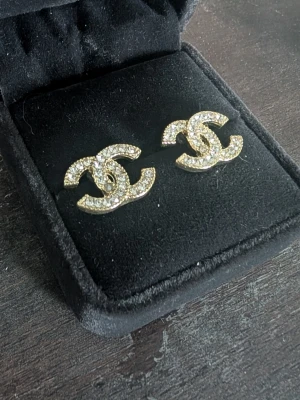 Guld cc örhängen med stenar - Snygga cc örhängen i guldtonad metall med glittrande stenar i form av två överlappande C. Perfekta för dig som gillar statement-smycken och vill ha något som sticker ut. Klassisk och trendig design som passar till många olika stilar.