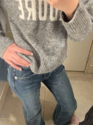 Grå stickad tröja - Mysig grå stickad tröja med vit texten 'ADORE' framtill. Tröjan har rund halsringning, långa ärmar och ribbade muddar vid ärmslut och nederkant. Säljer pga att den inte används 
