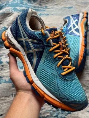 Blåa Asics sneakers med orange detaljer - Snygga sneakers från Asics i blå mesh med orange och vita detaljer samt orange snören. Skorna har en sportig look med ventilerande material och robust sula som ger bra grepp. Perfekta för dig som gillar färg och vill sticka ut. Jag tycker att de är lite små i storleken och snarare typ storlek 38-38,5.