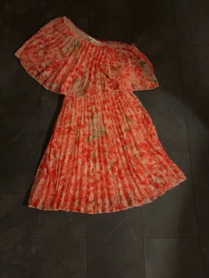 Blommig offshoulder klänning H&M - Säljer en blommig offshoulder klänning från H&M i storlek XXS. Klänningen har volang upptill, plisserad kjol och ett färgstarkt mönster i rosa, rött och grönt. Perfekt för sommarens alla tillfällen!