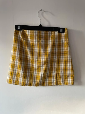 Gul och vit rutig kortkjol - Säljer en trendig kortkjol med gult och vitt rutmönster. Kjolen har en rak passform och dragkedja bak. Materialet känns lätt och passar bra till varmare dagar.