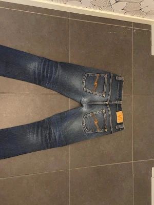 Blå Nudie jeans - Snygga blå jeans slim fit. Jeansen har en rak passform och coola slitningar framtill samt broderade detaljer på bakfickorna. Tillverkade i denim med en autentisk tvätt för en avslappnad look.