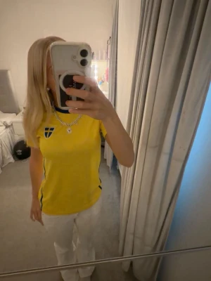 Gul Sverige fotbollströja nr 10 - Säljer en gul fotbollströja med blå detaljer och Sveriges landslagsemblem på bröstet. På ryggen står det 'SWEDEN' och siffran 10 i blått. Tröjan har rund hals och korta ärmar, perfekt för match eller supporterhäng.