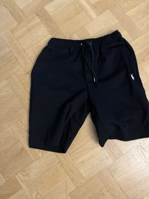 Ralph lauren shorts  - Svarta shorts med elastisk midja och snörning framtill. Klassisk rak passform och diskret logga på vänster ben. Perfekta för sommaren och tillverkade i mjukt bomullsmaterial för extra komfort.