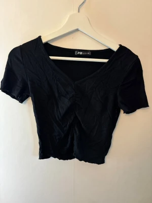 Svart croppad v-ringad topp - En svart croppad topp med v-ringning och korta ärmar. Toppen har en enkel och stilren design, perfekt att matcha med olika outfits. Tillverkad i mjukt material som känns bekvämt mot huden.