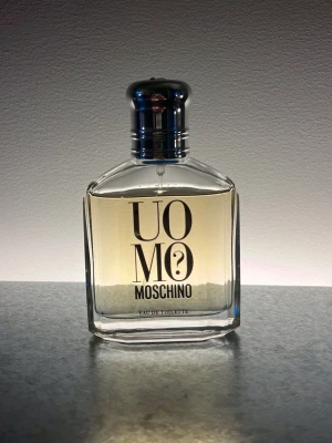 Moschino Uomo? Eau de Toilette 75ml - Moschino Uomo Eau de Toilette i en elegant, transparent glasflaska med silverfärgad metallkork. Flaskan har en stilren design med svart text och innehåller en ljusgul vätska. Perfekt för dig som gillar klassiska och fräscha dofter. Se bild för mängd kvar.