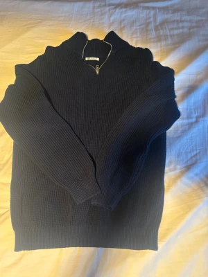 Mörkblå stickad halvzip tröja - Mörkblå stickad tröja med halvzip och hög krage. Tröjan har ribbstickade muddar vid ärmslut och nederkant. Perfekt för lager på lager och ger en clean look till din outfit.