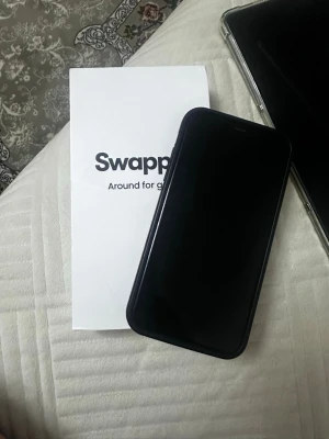Svart iPhone 11 64gb  med skal - Säljer en svart iPhone 11 från swapie olåst med 64gb, med stilren design och rundade kanter där de finns skavanker som syns på bilder. Telefonen har dubbla kameror på baksidan och kommer med ett svart skal.  Den har små repor på både fram och baksida.Tillverkad i glas och metall, perfekt för dig som gillar en modern look. Obs det är inte så högt ljudvolym på telefonen. Batterihälsa 75%