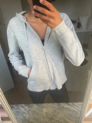 Ljusgrå zip hoodie med huva - Ljusgrå hoodie med dragkedja och huva. Klassisk modell med fickor framtill och ribbade muddar vid ärmslut och nederkant. Perfekt för en avslappnad och enkel stil. Tillverkad i mjukt sweatshirtmaterial. Lite små fläckar men annars mycket fin och bra kvalitet. Säljer då den ej kommer till användning. 