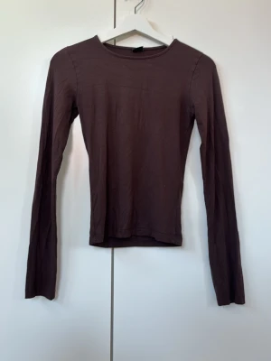 Brun långärmad topp Gina Tricot - Säljer en enkel och stilren brun långärmad topp från Gina Tricot i storlek XS. Toppen har rund halsringning och är gjord i ett mjukt, stretchigt material som sitter tajt mot kroppen. Perfekt att matcha med jeans eller kjol.
