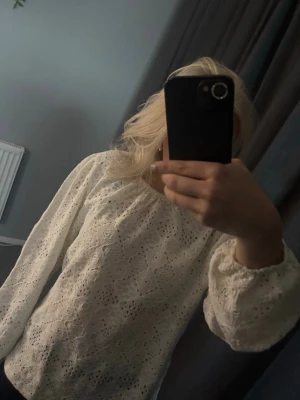 Vit spetsblus från Mywear - Söt vit spetsblus från Mywear med långärmad design och romantiskt hålmönster. Blusen har rund halsringning och puffiga ärmar med resår vid ärmslut. Perfekt för en trendig och feminin look.