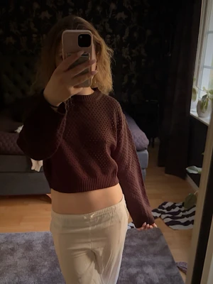 Stickad tröja med hålmönster - Säljer en svart stickad cropped tröja med hålmönster och långa ärmar. Tröjan har ribbade muddar vid ärmslut och nederkant samt en rund halsringning. Perfekt för lager på lager och ger en avslappnad men trendig look.