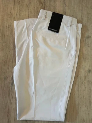 Vita golfbyxor från J.Lindeberg - Stilrena vita golfbyxor från J.Lindeberg med rak passform och bälteshällor. Byxorna har klassiska fickor och är tillverkade i ett lätt och stretchigt material som ger en bekväm känsla. Perfekta för en 18-håls runda på banan. Helt oanvända med prislapp. Modellen heter: Elof golf pant och storleken är: 32/32