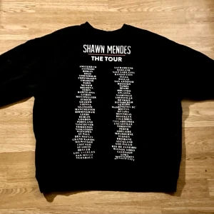 Shawn Mendes The Tour - Sweatshirt  - Säljer en svart Shawn Mendes The Tour 2019 sweatshirt med en ros på framsidan och  turnéstäder tryckta på ryggen. Från H&M Divided i storlek Medium(lite stor i storleken). Den har en klassisk passform och är perfekt för dig som gillar musikmerch eller Shawn Mendes och vill sticka ut med en snygg och bekväm tröja. Den är bara smutsig för den har legat på golvet. Använd ett fåtal gånger bara. Säljes pga används inte något mer🤩🙌🏻