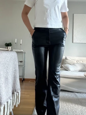 Svarta skinnbyxor från madlady - Snygga svarta byxor i skinnimitation med utsvängda ben och hög midja. Byxorna har en stilren look med fickor fram och dragkedja. Perfekta för dig som vill ha en trendig och edgy stil. Bra skick från madlady