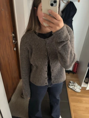 Brun fluffig kofta med knappar - Mysig brun kofta med fluffig textur och rund halsringning. Koftan har långa ärmar och stängs med små knappar framtill. Perfekt att slänga över en t-shirt för en avslappnad look.