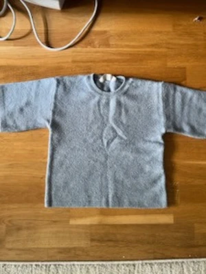 Ljusblå stickad tröja  - En enkel och stilren ljusblå stickad tröja med rund hals och raka ärmar. Tröjan har en mjuk och fluffig struktur, perfekt för kyliga dagar. Passar både tjejer och killar som gillar en clean look.