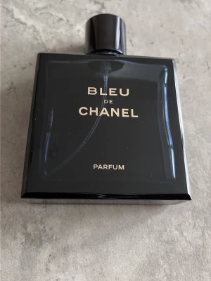 Bleu de Chanel Parfum - Säljer en tom Bleu de Chanel Parfum i en elegant mörkblå glasflaska med guldfärgad text och svart lock med Chanel-loggan på toppen. Flaskan har en stilren, fyrkantig form och utstrålar lyxig känsla. Perfekt för dig som gillar exklusiva dofter.