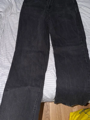 Svarta vida jeans med rå kant - Säljer ett par svarta jeans med bred passform och rå, avklippt kant nedtill (de skall vara så). Perfekta för en avslappnad och trendig look.