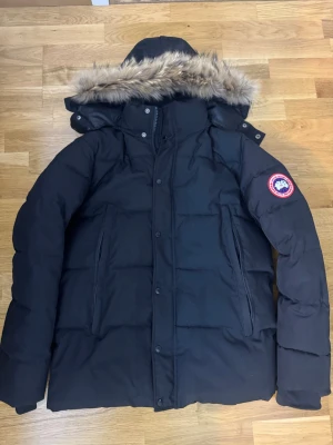 Svart dunjacka  - Säljer en svart dunjacka med avtagbar huva och fuskpäls. Jackan har två stora fickor framtill. Perfekt för kalla vinterdagar och riktigt varm tack vare dunfyllningen.