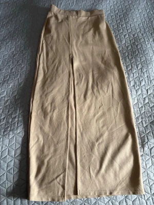 Beige rak kjol med slits - En beige rak kjol i mjukt tyg med enkel design och slits framtill. Kjolen har en hög midja och är helfärgad utan synliga detaljer eller mönster. Perfekt för en stilren och minimalistisk look.