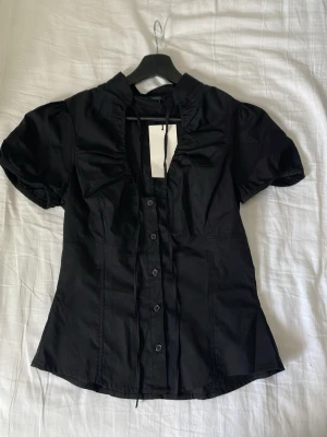 Svart Zara blus med puffärm  - Snygg svart Zara blus med puffiga korta ärmar och volangkant längs knäppningen. Figurnära passform och liten ståkrage ger en trendig look. Prislapp kvar och endast provad!!!💓
