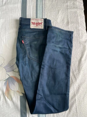 Mörkblå Levi's jeans med rak passform - Säljer ett par klassiska mörkblå jeans från Levi's med rak passform och fem fickor. Jeansen har en snygg tvätt och detaljer som den ikoniska röda Levi's-lappen på bakfickan. Tillverkade i slitstark denim som passar perfekt till alla tillfällen.