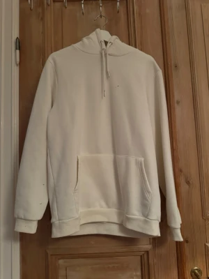 Vit hoodie med ficka och huva - Säljer en enkel och stilren vit hoodie med stor magficka och dragsko i huvan. Hoodien har långa ärmar och ribbade muddar vid ärmslut och nederkant. Perfekt för en avslappnad och clean look.