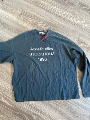 Svart långärmad tröja Acne Studios - Cool svart långärmad tröja från Acne Studios med trycket 'STOCKHOLM 1996' på bröstet. Tröjan har en avslappnad passform och rund halsringning. Perfekt för dig som gillar streetwear och enkel stil.