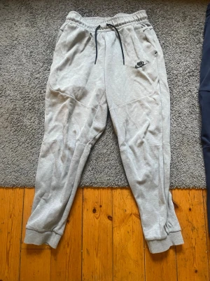 Gråa mjukisbyxor från Nike XL - Snygga grå mjukisbyxor från Nike med svart logga på vänster sida. Byxorna har resår i midjan med svart dragsko och muddar vid bensluten. Tillverkade i mjukt och bekvämt material, perfekta för chill dagar eller träning. ( passar från storlek S-M)
