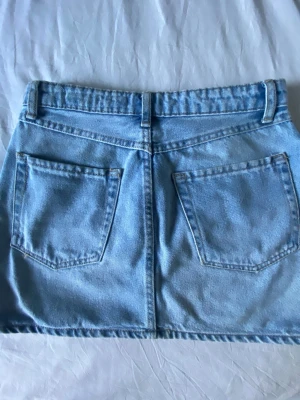 Ljusblå jeanskjol med fickor - Snygg ljusblå jeanskjol i klassisk modell med fem fickor, bälteshällor och dragkedja framtill. Kjolen har en rak passform och är perfekt för dig som gillar en enkel men trendig stil. Passar till allt från sneakers till boots.