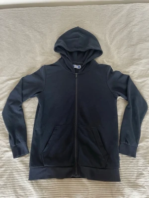 Mörk blå zip hoodie med huva - En stilren svart hoodie med dragkedja framtill och två fickor. Klassisk modell med huva och långa ärmar. Tillverkad i mjukt bomullsmaterial som är skönt att bära. Perfekt för en avslappnad look. Tröjan är nopprig där av priset!