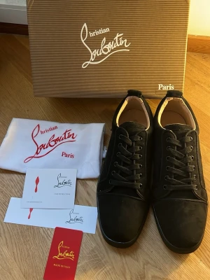 Svarta sneakers från Christian Louboutin - Snygga svarta sneakers från Christian Louboutin med klassisk röd sula och diskret logga. Skorna har en låg profil, rund tå och svarta skosnören. Tillverkade i mocka och läder för en lyxig känsla. Perfekta för dig som vill sticka ut med exklusiva detaljer.