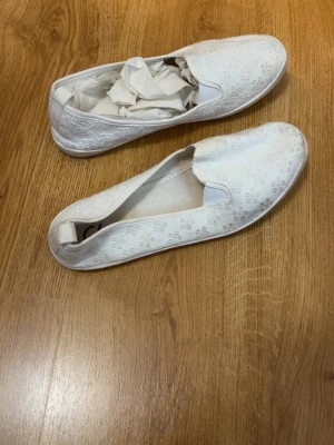 Vita ballerinaskor med blommönster - Säljer ett par vita ballerinaskor från Clou med sött blommönster i tyget. Skorna har rund tå och är tillverkade i textilmaterial. Perfekta för en avslappnad och stilren look.