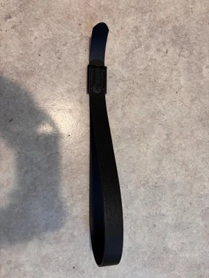 Svart skärp från Armani i skinn - Snyggt svart skärp från Armani i äkta skinn med en stilren, matt svart spänne där loggan syns tydligt. Bältet har en klassisk design som passar till många olika outfits och ger en clean look.