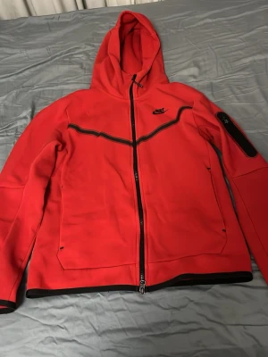Röd Nike hoodie med dragkedja - Snygg röd hoodie från Nike med hel dragkedja och svarta detaljer. Huva, fickor på sidorna och en extra ficka med dragkedja på ärmen. Perfekt för en sportig och avslappnad stil. Priset kan diskuteras vid snabb affär. Det är s men passar som M 