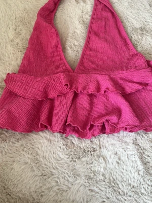 Rosa volang topp med halterneck - Säljer en snygg rosa halterneck topp med volangdetaljer. Toppen är ärmlös och har en croppad passform som passar perfekt till sommaren. Materialet är ribbat och stretchigt för en bekväm känsla. Den är cirka storlek S men fungerar toppen för XS och M också! Den har en öppen rygg vilket gör den perfekt för finare tillfällen men även när du ska gå på stan💞 Vid frågor skriv och jag är öppen för prisförslag!