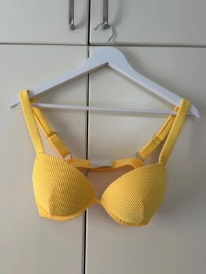 Bikini set - Snygg gul bikiniöverdel med ribbad struktur och breda axelband. Bikinin har vadderade kupor och justerbara band för bästa passform. Perfekt för soliga dagar på stranden eller vid poolen.