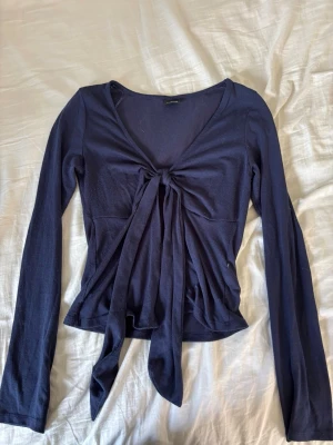 Mörkblå långärmad topp med knyt - Snygg mörkblå långärmad topp med v-ringning och knyt framtill. Toppen har en croppad passform och är tillverkad i mjukt bomullsmaterial. Perfekt att styla med jeans eller kjol för en trendig look.
