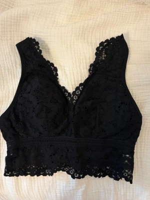 Svart spetsbralette med bred kant - Snygg svart bralette i spets med bred kant nertill och v-ringad fram och bak. Braletten har blommigt spetsmönster och breda axelband för extra komfort. Perfekt att ha under en kavaj