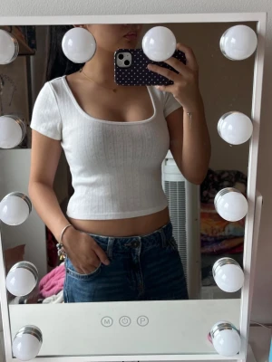 Vit croppad pointelle topp - Säljer en vit croppad topp med pointelle struktur och fyrkantig ringning. Toppen har korta ärmar och sitter tight mot kroppen, perfekt till jeans eller kjol. Enkel och stilren design som passar till många olika looks.