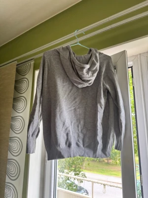 Grå hoodie - En stilren grå hoodie med huvaTillverkad i mjukt material och har ribbade muddar vid ärmslut och nederkant. Perfekt för en avslappnad look och enkel att matcha med andra plagg. Hör gärna av er vid mer intresse!