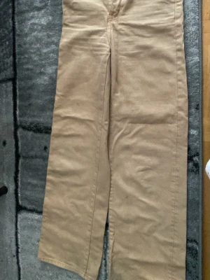 Beiga raka jeans - Säljer ett par beiga jeans med rak passform och klassisk look. Byxorna har normal midja och är sydda i ett mjukt bomullstyg som känns skönt mot huden. Perfekta för dig som gillar en clean och enkel stil.